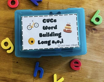 May include: A blue plastic storage box with a white label that says "CVCe Word Building Long a,o,i" and has pictures of a bicycle, a honeycomb, and a birthday cake. The box is filled with colourful magnetic letters.