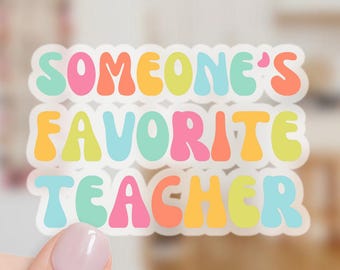May include: A colorful sticker with the text "SOMEONE'S FAVORITE TEACHER" in a retro font. The sticker features a white border and is held by a hand with a gold ring. The text is in shades of pink, orange, yellow, green, and blue.