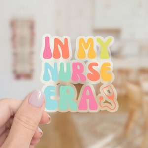 May include: A colorful sticker with the text "In My Nurse Era" in a retro font. A stethoscope is included in the design.