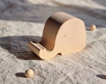 May include: A wooden elephant phone stand made of light wood. The stand has a small hole for the phone to rest in.