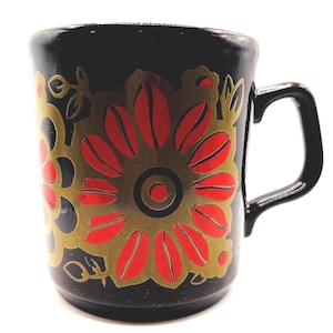 May include: Black ceramic mug with a floral design in red and gold. The mug has a rounded shape and a black handle. The floral pattern is a prominent design element, adding a decorative touch to the mug.