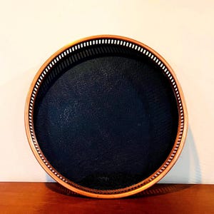 May include: A round serving tray with a dark blue interior and a decorative rim. The rim is a light brown color with a white dotted pattern. The tray is sitting on a wooden surface.