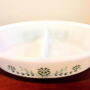 May include: White, oval-shaped divided serving dish with a green floral pattern. The dish is split into two sections and features a decorative design of flowers and leaves along the bottom edge. The dish is made of a glossy, opaque material.