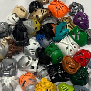 Op de afbeelding: Een verzameling kleurrijke plastic maskers in verschillende vormen en ontwerpen. De maskers zijn in tinten rood, groen, blauw, oranje, zilver, zwart en goud. Sommige maskers hebben ingewikkelde details en patronen, andere zijn eenvoudiger.