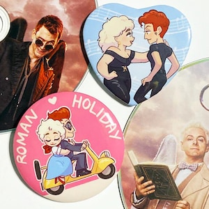 May include: A selection of pin badges with cartoon illustrations. One badge is heart-shaped with two figures, another is round with the text "ROMAN HOLIDAY", and the third shows two figures on a scooter. The background includes images on CDs.