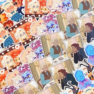 May include: A collection of colorful stickers featuring cartoon illustrations. Some stickers depict characters in various scenes, while others showcase film strip designs with cute characters. The stickers are in shades of blue, orange, and pink.