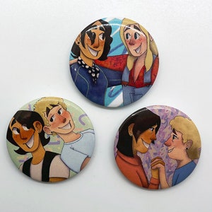 May include: Four round pins with colourful illustrations of people. The first pin features two people with dark hair, one wearing a blue jacket and the other wearing a red and blue jacket. The second pin features two people with light hair, one wearing a blue shirt and the other wearing a light blue shirt. The third pin features two people with dark hair, one wearing a red shirt and the other wearing a blue shirt. The fourth pin features two people with light hair, one wearing a red shirt and the other wearing a blue shirt.