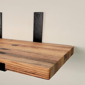 Peut inclure: Étagère flottante en bois avec un fini grain de bois naturel. L'étagère est soutenue par deux supports métalliques noirs au mur et un support métallique noir en bas. L'étagère mesure environ 30 cm de profondeur.