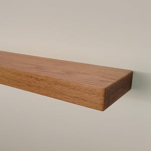 May include: A rectangular, floating wooden shelf, showcasing a natural wood grain pattern. The shelf is a warm brown color and appears to be mounted on a neutral-toned wall. This shelf is ideal for displaying decor or storing items.
