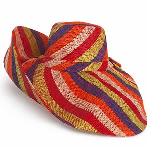 May include: A wide-brimmed straw hat featuring a vibrant, multi-coloured striped pattern in shades of red, orange, yellow, and purple. The hat has a woven texture and a structured crown with a slightly upturned brim on one side, showcasing a consistent diagonal stripe design throughout the entire surface.