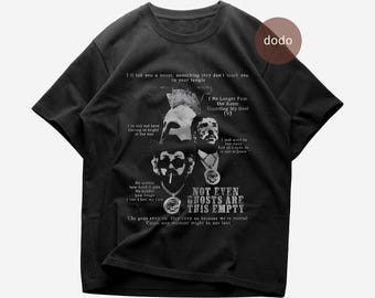 Puede incluir: Una camiseta negra de manga corta con un estampado gráfico que incluye varios retratos, letras de canciones y el texto "I No Longer Fear the Razor Guarding My Heel (V)" y "NOT EVEN GHOSTS ARE THIS EMPTY" en un estilo de fuente blanco.