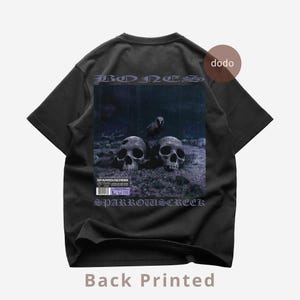 Könnte beinhalten: Schwarzes T-Shirt mit einem Grafikdruck mit zwei Totenköpfen und einer Krähe unter dem Wort "BONES". Der Text "SPARROWSCREEK" ist darunter gedruckt. Die Worte "Back Printed" sind unten gedruckt.