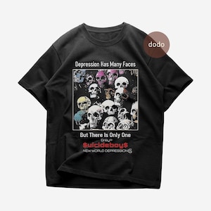 Op de afbeelding: Zwart T-shirt met een afbeelding van meerdere schedels in verschillende kleuren. De tekst "Depression Has Many Faces, But There Is Only One" staat boven de afbeelding. Het shirt heeft ook de tekst "$uicideboy$ NEW WORLD DEPRESSION".
