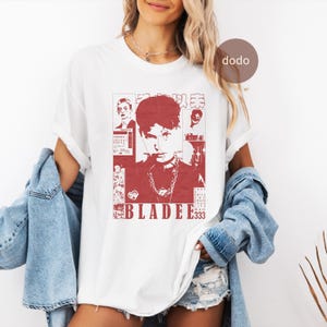 Puede incluir: Camiseta blanca con un diseño gráfico rojo. El diseño presenta un retrato de una persona con la palabra "BLADEE333" y otro texto. La camiseta tiene mangas cortas y cuello redondo.