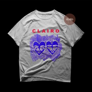 May include: A light gray short-sleeve t-shirt featuring the red text CLAIRO above a graphic of two blue heart-shaped faces surrounded by blue abstract line patterns. A small brown circle with the white text dodo is in the upper right corner.