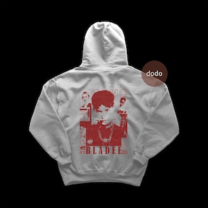 Puede incluir: Una sudadera con capucha gris claro con un gráfico rojo en la espalda. El gráfico presenta un retrato de una persona con una cadena y el texto "BLADEE333". La sudadera tiene un cordón y un bolsillo de canguro.