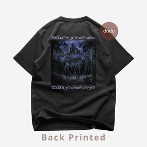 Könnte beinhalten: Schwarzes T-Shirt mit einem grafischen Aufdruck auf der Rückseite, der zwei Figuren zeigt, die auf ein Schloss in einem Wald zugehen. Die Wörter "BONES" und "DUNGEON" sind oberhalb und unterhalb der Grafik aufgedruckt. Die Worte "Back Printed" sind unten aufgedruckt.