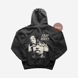 May include: Black hoodie with a graphic of ASAP Rocky in black and white. The hoodie has a hood and the text "ASAP ROCKY" printed on the back. The hoodie is made of a soft material.