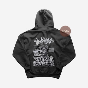 May include: Black hoodie with a graphic design on the back. The design includes the word "BROOKLYN" in a graffiti style, a portrait of Rakim Athelaston Mayers, and other text elements. The hoodie has a hood and a kangaroo pocket.