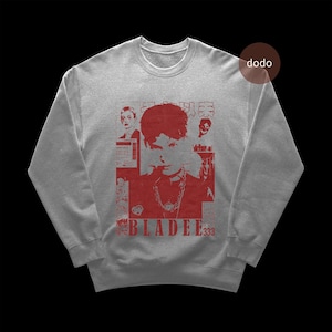 Puede incluir: Sudadera gris jaspeada con un diseño gráfico rojo. El diseño incluye un retrato, el texto "BLADEE 333" y caracteres japoneses. La sudadera tiene cuello redondo y mangas largas.