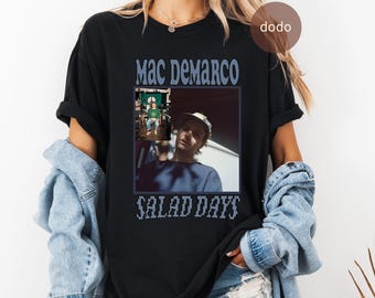May include: Black t-shirt featuring a photo of Mac DeMarco with the text "Mac DeMarco" above and "Salad Days" below the image. The image is a square with a photo of Mac DeMarco.
