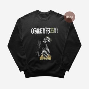 May include: Black sweatshirt featuring a detailed illustration of a skeleton with flames at the bottom. The text "GREYBOY" is above the skeleton, with an anarchy symbol and the year "2023" on the right.