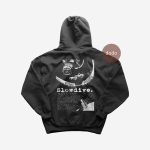 May include: Dark gray hoodie with a white graphic on the back featuring a space station, astronaut, and the text "Slowdive." The text "May 17, 1993" is also included. The hoodie has a hood and a kangaroo pocket.
