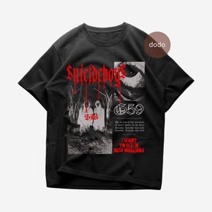 Op de afbeelding: Zwart t-shirt met rode gotische tekst "Suicideboys". Het ontwerp bevat een afbeelding van twee figuren in witte gewaden, een oog en de tekst "659". De tekst "I WANT TO DIE IN NEW ORLEANS" is ook aanwezig.