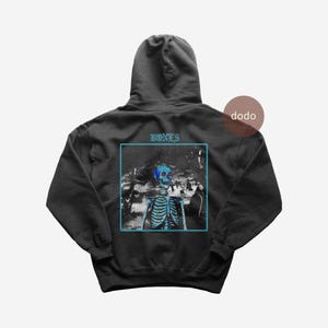 Könnte beinhalten: Schwarzer Kapuzenpullover mit einer Skelettgrafik in einem blauen Quadrat, darüber steht das Wort "BONES". Das Skelett hat einen blauen Schädel und Brustkorb. Der Hoodie hat eine Kapuze und eine Kängurutasche.
