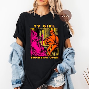 May include: Black t-shirt with a graphic print featuring two figures in a vintage style. The text "TV GIRL" is above the image, and "SUMMER'S OVER" is below. The figures are in bright pink and orange hues.