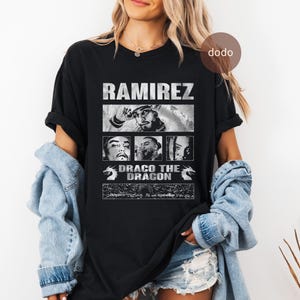 May include: Black t-shirt featuring the name "RAMIREZ" above three grayscale images of a man. Below the images is the text "DRACO THE DRAGON" with dragon illustrations on each side. The shirt is worn by a person.