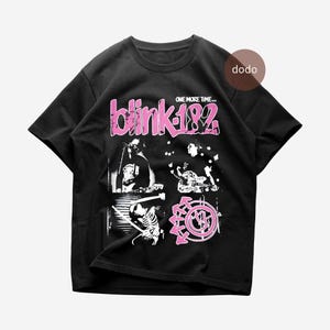 Peut inclure: Un t-shirt noir à manches courtes avec une impression graphique incluant le texte "blink-182" et "ONE MORE TIME..." en rose. Le motif présente des images en noir et blanc de musiciens, un squelette et un logo circulaire rose à flèches.