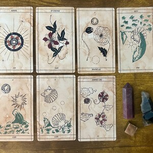 May include: Seven rectangular tarot cards with a vintage parchment-style background and ink-style illustrations, arranged in two rows. Beside the cards are three crystals: a tall pink hexagonal point, a dark jagged stone, and a small metallic cube.