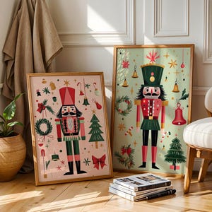 May include: Two framed prints featuring festive nutcracker illustrations. The artwork showcases a nutcracker soldier in red, green, and black, surrounded by Christmas-themed elements like bells, wreaths, and trees. The frames are a warm wood tone.