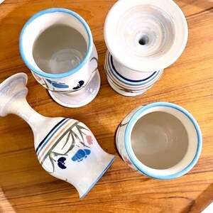 Puede incluir: Cuatro tazas de cerámica con diseños florales azules y blancos. Las tazas tienen un esmalte blanco y están decoradas con flores azules y blancas. Las tazas están sobre una bandeja de madera.