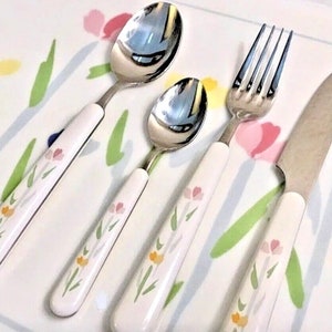 May include: A set of four floral patterned silverware pieces, including a fork, knife, and two spoons. The handles are white with a floral design in pink, yellow, and green.