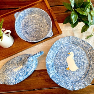 May include: A set of blue and white ceramic dishes with a speckled pattern. The dishes include a large platter with a white duck design, a smaller platter, and a bowl.
