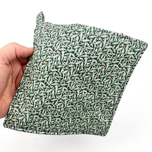 May include: Green pot holder with a white and brown floral pattern. The pot holder is made of fabric and has a loop handle.
