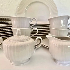 May include: A set of white porcelain teacups, saucers, and a sugar bowl with a lid. The cups and saucers have a fluted design and the sugar bowl has a smooth, rounded shape.