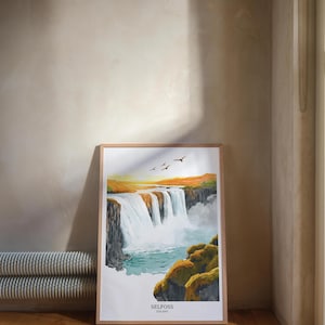 Puede incluir: Una impresión enmarcada de la cascada de Selfoss en Islandia. La obra de arte representa una cascada de agua blanca, sobre un fondo de tonos naranjas y amarillos. La impresión está en un marco de madera y se exhibe sobre un suelo de madera.