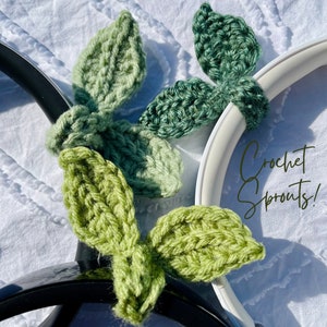 May include: Two sets of crocheted green leaf-shaped headphone charms. The charms are attached to a pair of headphones. The text "Crochet Sprouts!" is visible in the image.