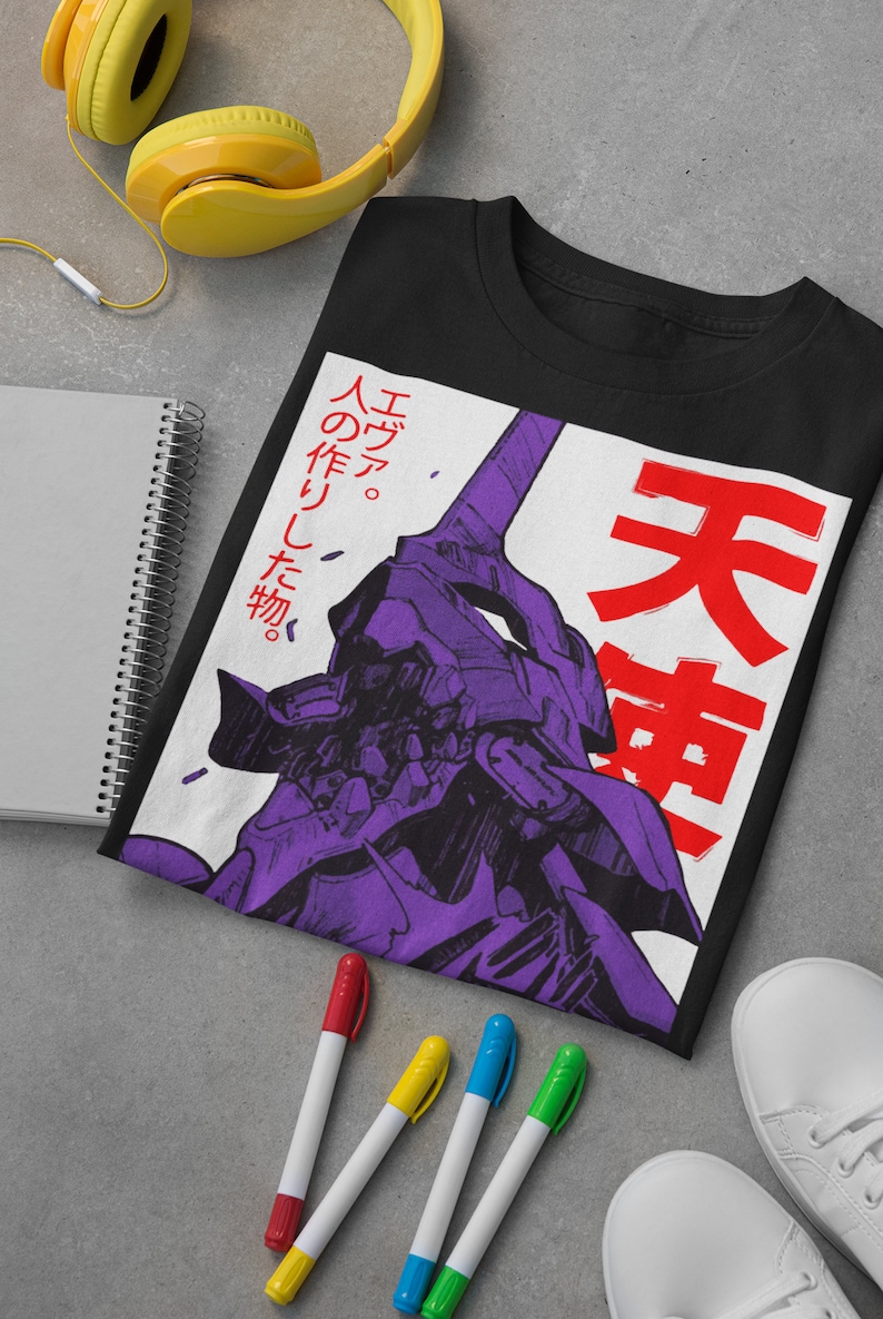 Może przedstawiać: Czarny T-shirt z białym nadrukiem przedstawiającym fioletowego robota z japońskim tekstem "エヴァ。 人の作りし物。 天  " w kolorze czerwonym.