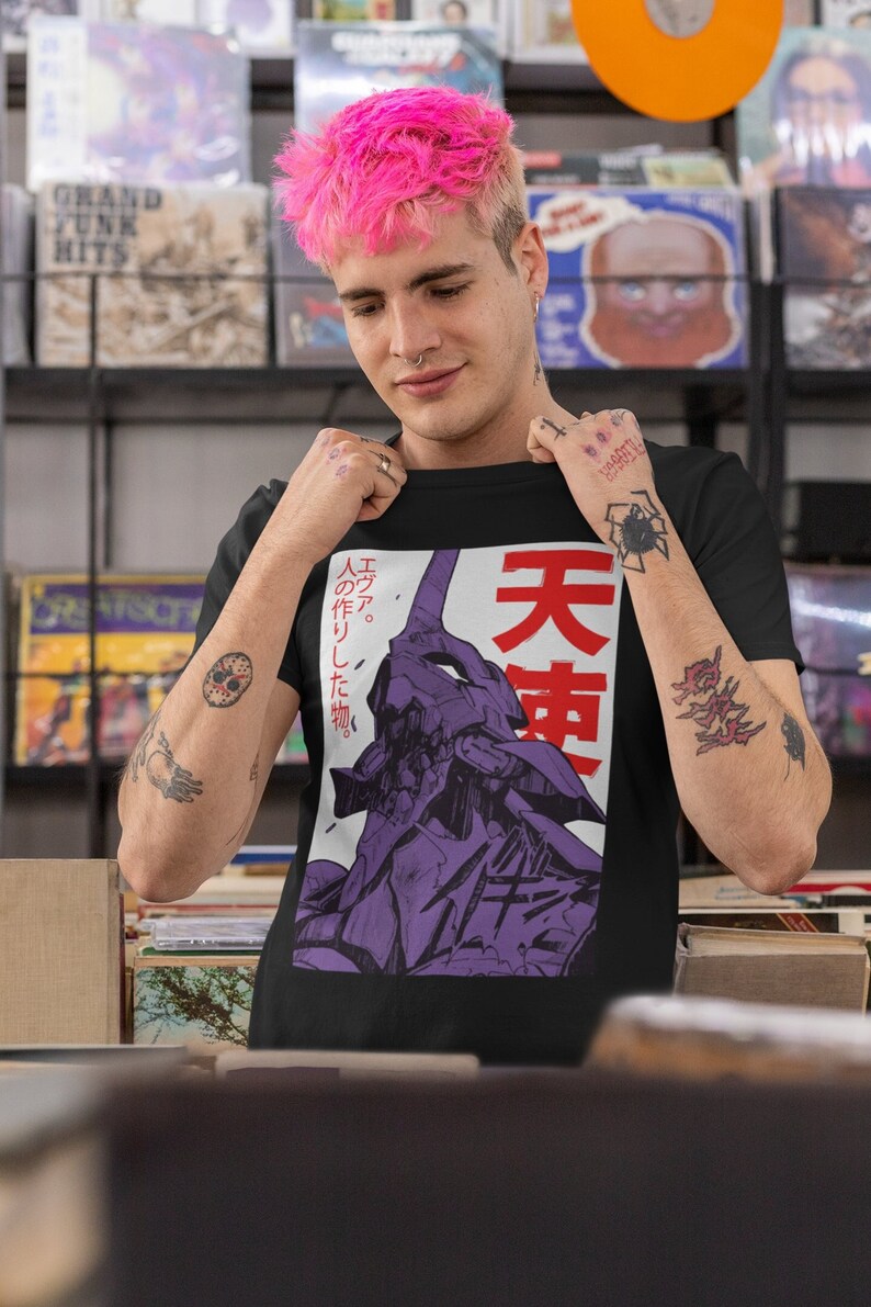 Może przedstawiać: Czarny T-shirt z nadrukiem graficznym fioletowego robota z japońskim tekstem "人エ. の作りし神." i "天使" w kolorze czerwonym. Osoba nosząca koszulkę ma r&oacute;żowe włosy i kolczyk w nosie.