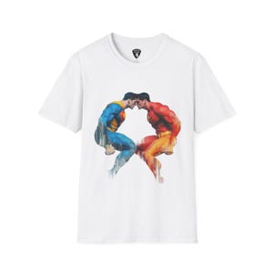 May include: White t-shirt featuring a graphic of two muscular figures in superhero costumes, one blue and yellow, the other red and orange, facing each other. The figures are set against a cityscape backdrop.