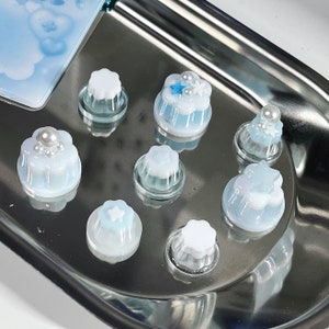 May include: A collection of seven small, white and blue cake decorations with pearl and star accents. The decorations are arranged on a silver tray.