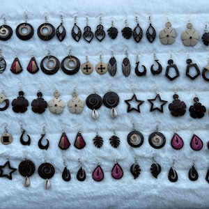 May include: A collection of 40 pairs of coconut shell earrings with various designs, including geometric shapes, flowers, and swirls. The earrings are made of natural coconut shell and have a brown color.