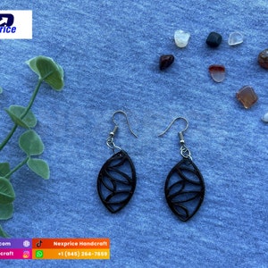 May include: A pair of black dangle earrings with a leaf-shaped design. The earrings are made of metal and have a silver finish. The earrings are hanging from a blue background.