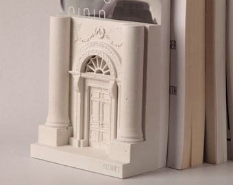 Puede incluir: Mantiene libros de yeso blanco en forma de puerta con columnas. Los sujetalibros sostienen una pila de libros con el título "fotograf-opin" visible en el libro superior.