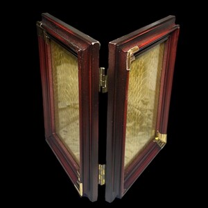 May include: A two-panel, hinged picture frame with a dark red wooden frame and gold-coloured corner accents. The frame is open, revealing a textured, golden-coloured interior. The hinges are gold-coloured.