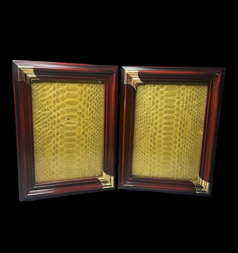 May include: Two rectangular picture frames with a dark red-brown wood finish and gold-coloured corner accents. The frames have a yellow, textured background, possibly faux snakeskin. The frames are displayed against a black background.